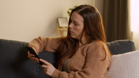 Woman-Sitting-On-Sofa-At-Home-Using-Mobile-Phone-To-Check-Social-Media-Message-And-Scrolling-Online-12